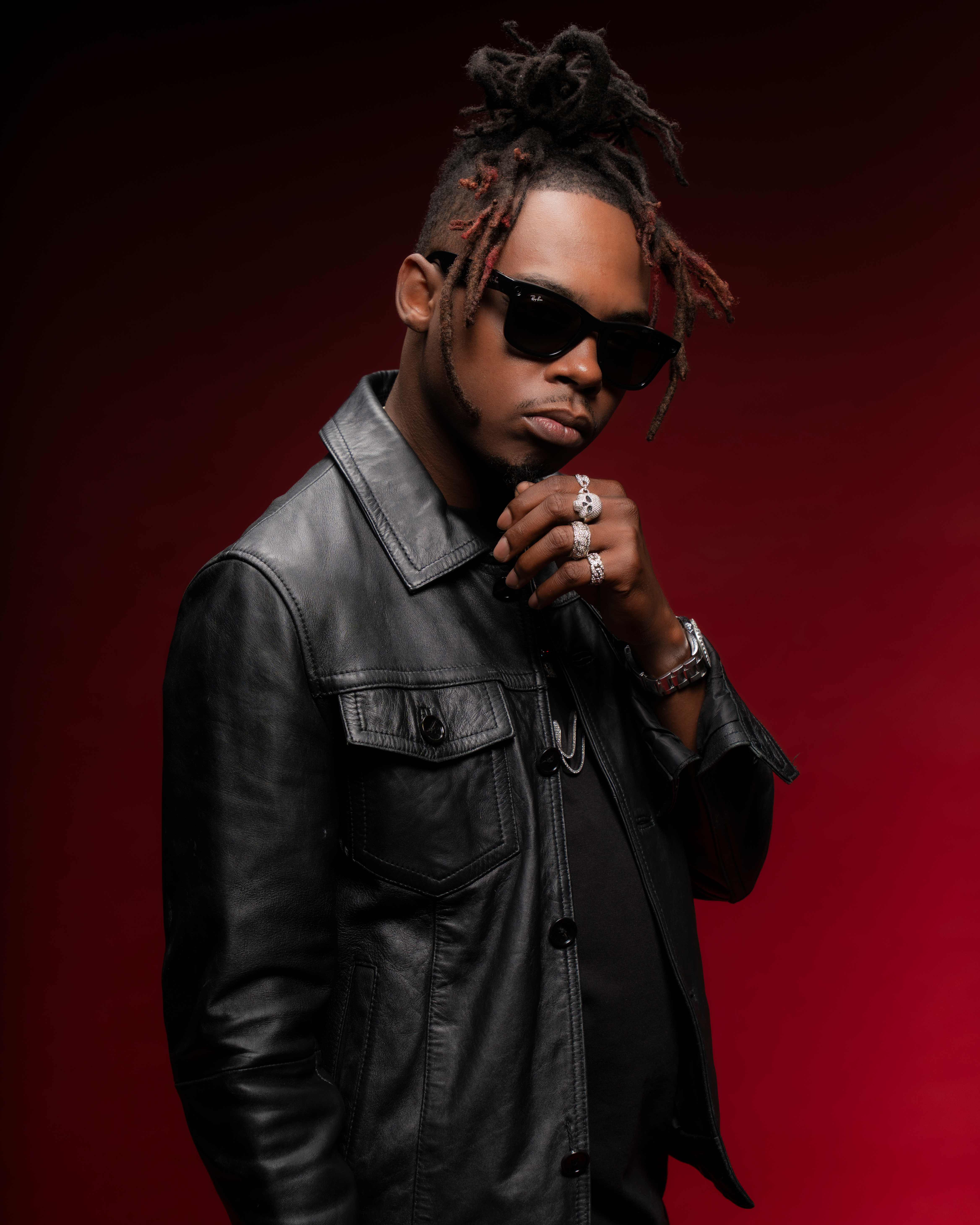 Trap Beckham in a black leather jacket and sunglasses against a deep red backdrop
